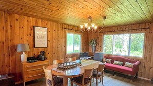 Interior de una cabaña de madera con una mesa de comedor, sillas, un sofá y una araña.