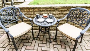 A patio with two metal chairs and a table, set against a stone wall. - Victoria House (Holmfirth)