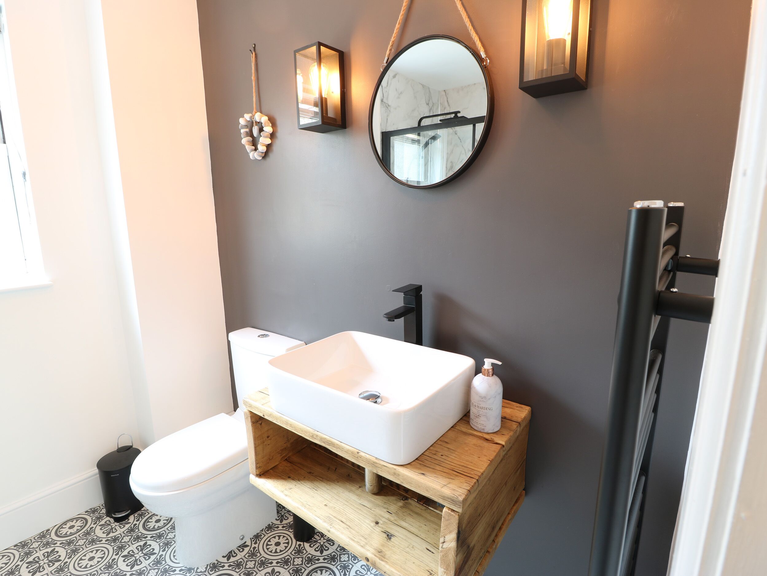 Un baño moderno con lavamanos blanco, tocador de madera y un espejo redondo.