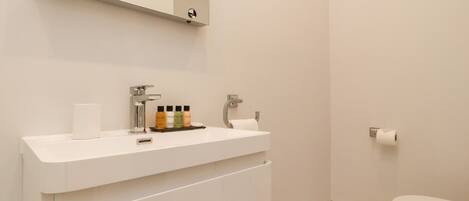A bathroom with a white sink, mirror, and toilet. There are toiletries on the sink and a towel hanging on the wall.