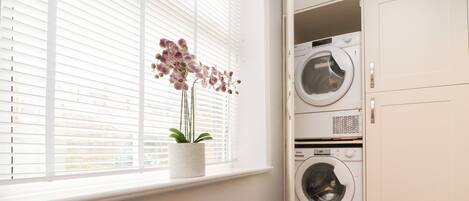 A laundry room with two stacked washing machines, a potted orchid on the windowsill, and white cabinetry.