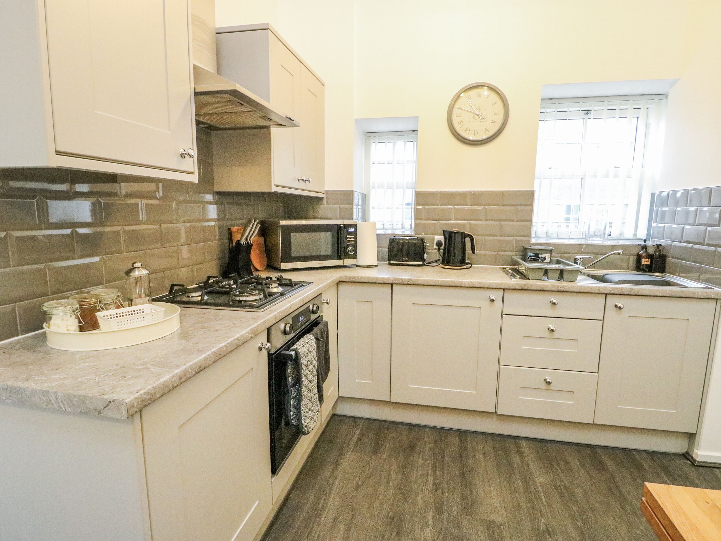 A kitchen with a gas stove, microwave, toaster, and a clock on the wall.