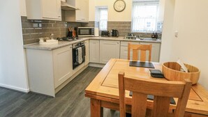 A compact kitchen with a dining area, featuring a microwave, stove, sink, and wooden chairs. - 2 Mountain View (Llangefni)