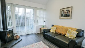 A living room with a black leather sofa, a patterned rug, a fireplace, and a large window with blinds. - 2 Mountain View (Llangefni)