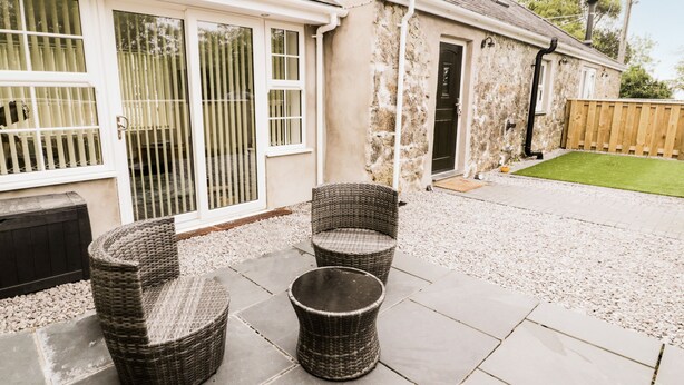 A patio area with wicker furniture and a stone floor. - 2 Mountain View (Llangefni)