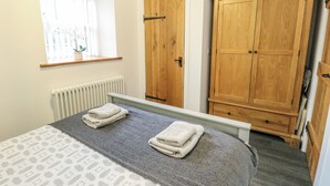 A bedroom with a bed, a window with blinds, a radiator, and wooden wardrobes. - 2 Mountain View (Llangefni)