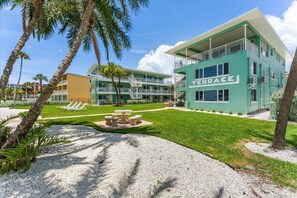 A multi-story hotel with a green facade, a terrace area with seating, and palm trees.