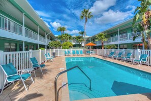 A pool area with a clear blue pool, white railings, and green chairs.