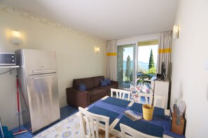 Un espacio habitable compacto con kitchenette, un sofá marrón, una mesa de comedor con sillas y vistas a través de un ventanal grande.