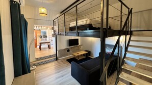 A modern, compact room with a bunk bed, a small table, and a sofa. There is a staircase leading to an upper level, and a hallway with a door leading to another room. - "Mas Thomasine <br>quiet romantic apartment in nature in Peillon (Peillon)