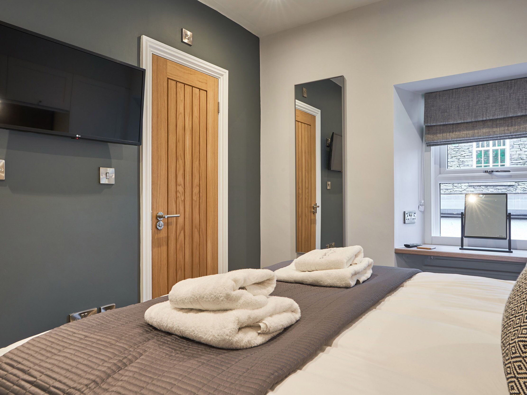 Een hotelkamer met een bed, een houten deur, een spiegel en een raam met uitzicht.