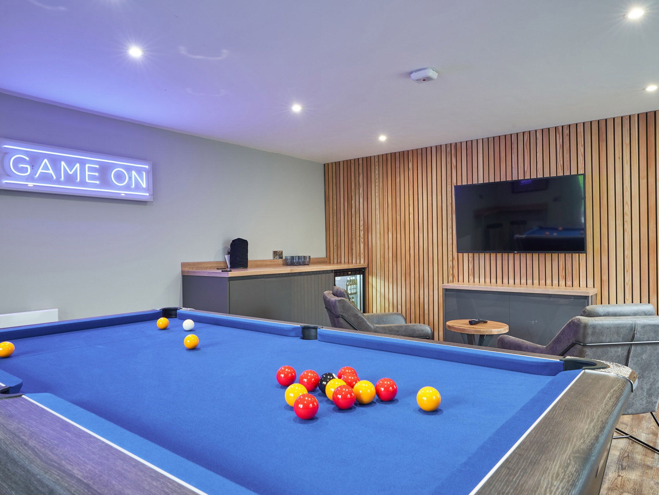 Una mesa de billar con bolas, una televisión y un cartel que dice "GAME ON".