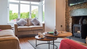 A cozy living room with a stone fireplace, a sofa with cushions, a coffee table, and a TV mounted on the wall. - Upper Sheriff's Place (Windermere)