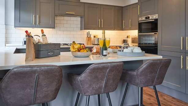 A modern kitchen with grey cabinets, a central island with bar stools, and pendant lighting. - Upper Sheriff's Place (Windermere)