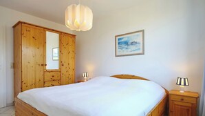 A bedroom with a wooden bed, a nightstand with a lamp, a wardrobe, and a painting on the wall. - Sünnslag Wohnung 064 (Ostseebad Boltenhagen)