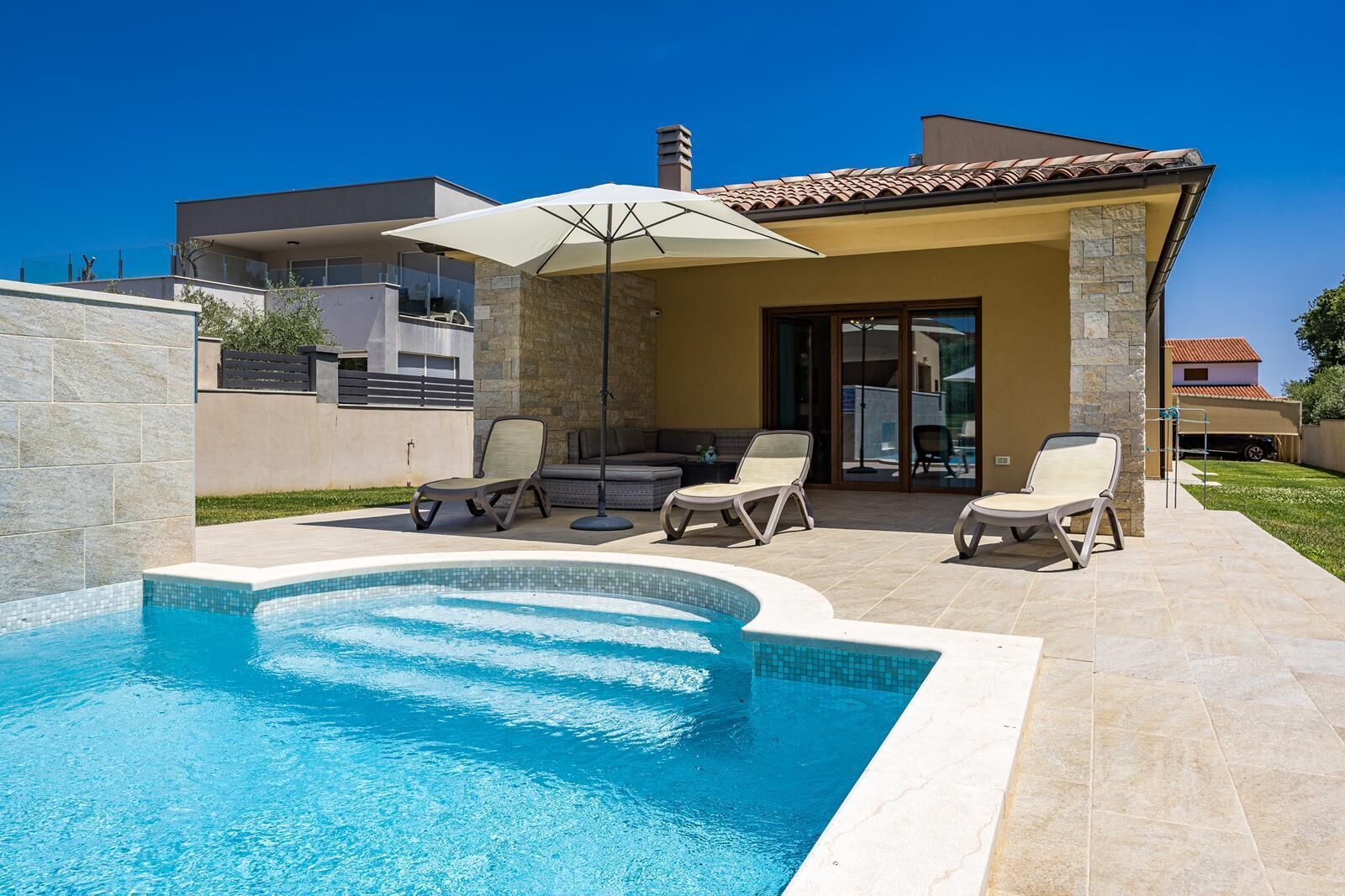 A swimming pool with lounge chairs and an umbrella, surrounded by stone walls and a tiled patio.