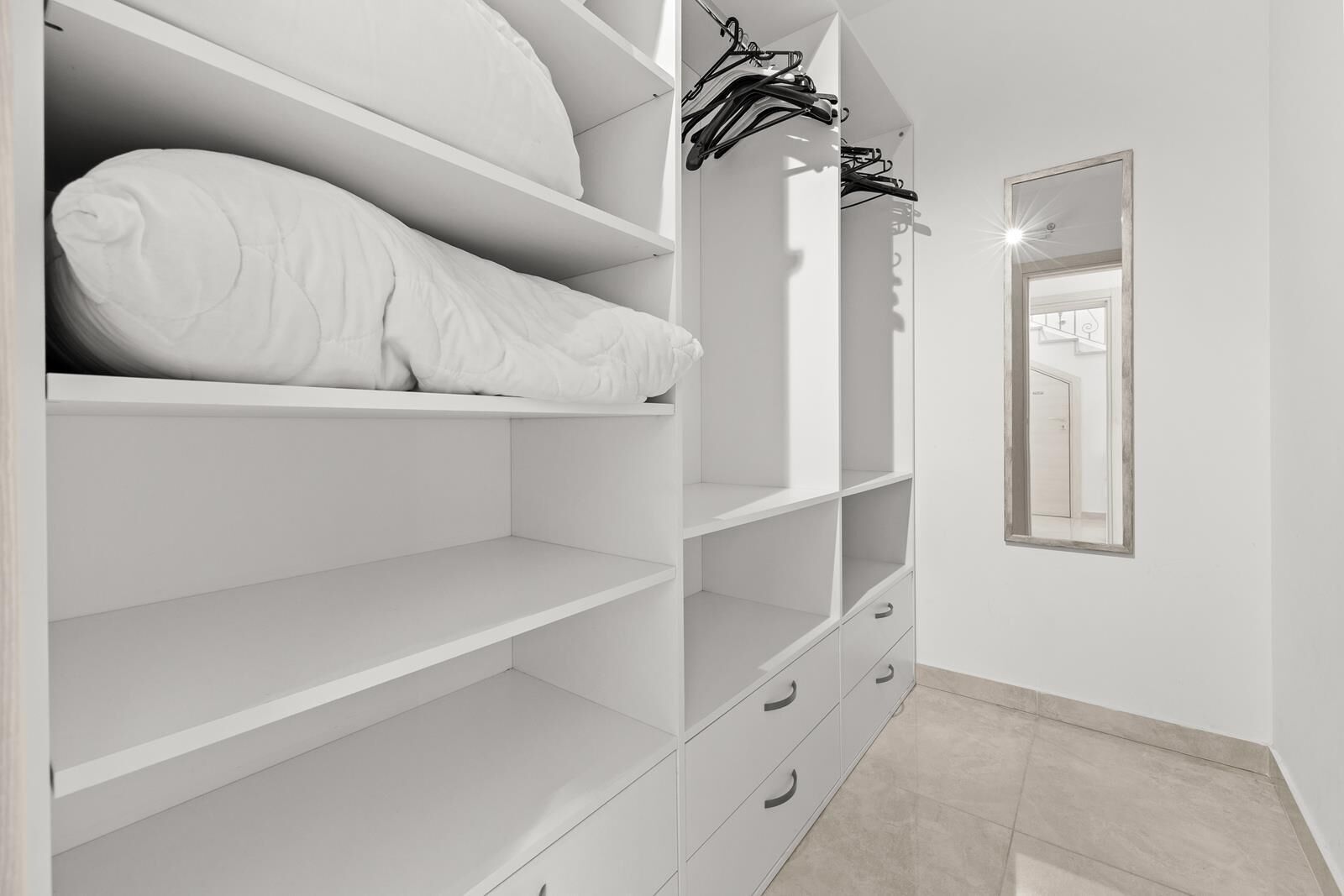 A white walk-in closet with shelves, a hanging rod, and a mirror.