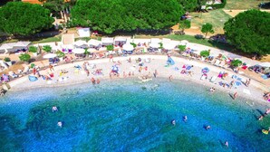 An aerial view of a beach with clear blue water, people swimming and sunbathing, and beach umbrellas. - Villa Markulin in village Šišan (Šišan)