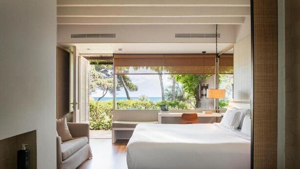 A modern bedroom with a large bed, a sitting area, and a view of the sea.