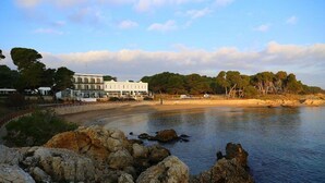 A coastal hotel with a large building, rocky shoreline, and trees in the background.