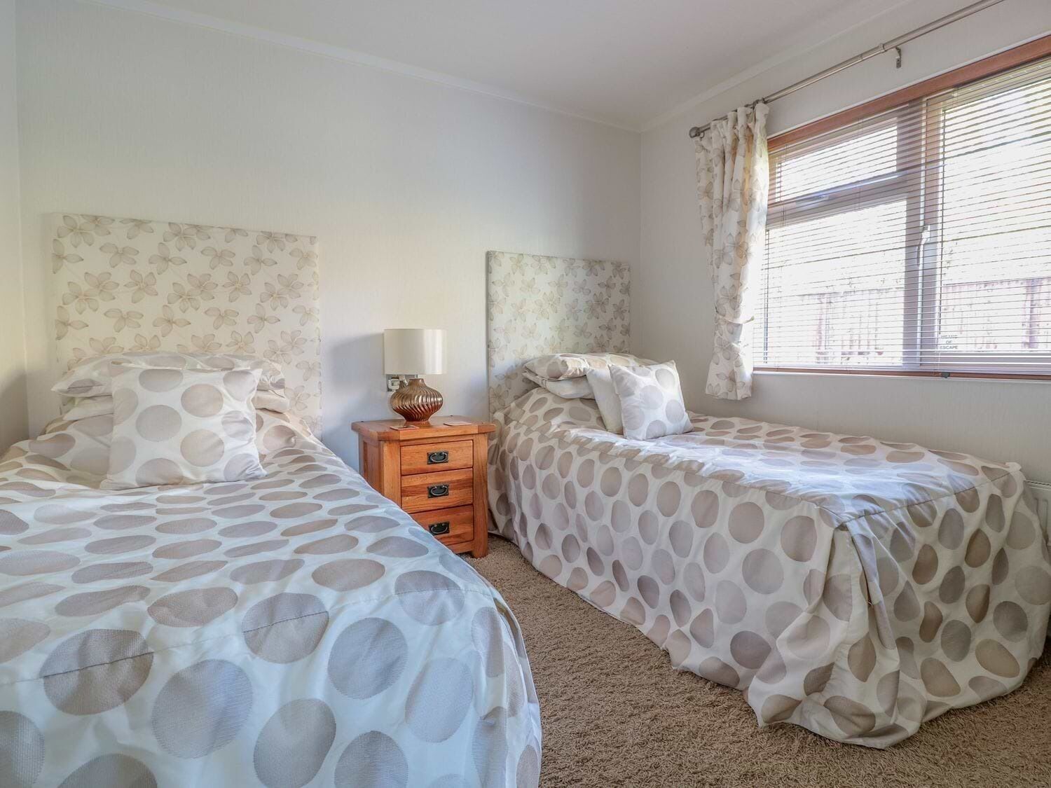 Un dormitorio con dos camas, una mesita de noche, una lámpara y una ventana con cortinas.