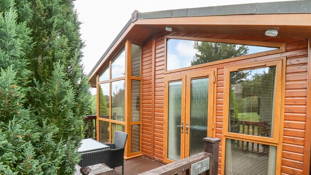 Eine Holzhütte mit großen Glasfenstern und -türen, einer Holzdiele und einem Schild mit der Aufschrift 'Oak Lodge'.