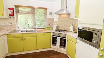 Una cocina con gabinetes verdes, una campana extractora de acero inoxidable, un microondas y una ventana con persianas.