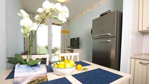 Una cocina con un refrigerador de acero inoxidable, una mesa de comedor con un bol de limones y una orquídea en maceta.