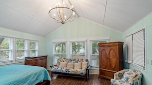 A bedroom with a bed, a sofa, a chair, a wardrobe, and a chandelier.