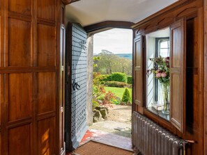 Une porte en bois s’ouvre sur un jardin offrant une vue sur les arbres et un ciel dégagé.