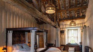 A traditional bedroom with a four-poster bed, a wooden headboard, a bedside table with a lamp, and a window with curtains. - Fernhill Castle (Keighley)