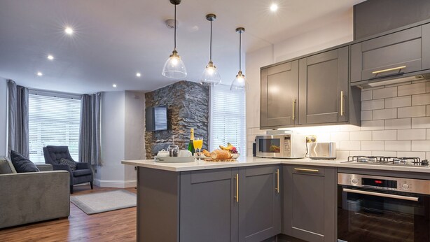 A modern kitchen with grey cabinets, a central island, a microwave, a toaster, and an oven. - Lower Sheriff's Place (Windermere)
