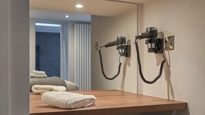 A bathroom with a wooden vanity, two hair dryers mounted on the wall, and a towel on the counter. - Lower Sheriff's Place (Windermere)