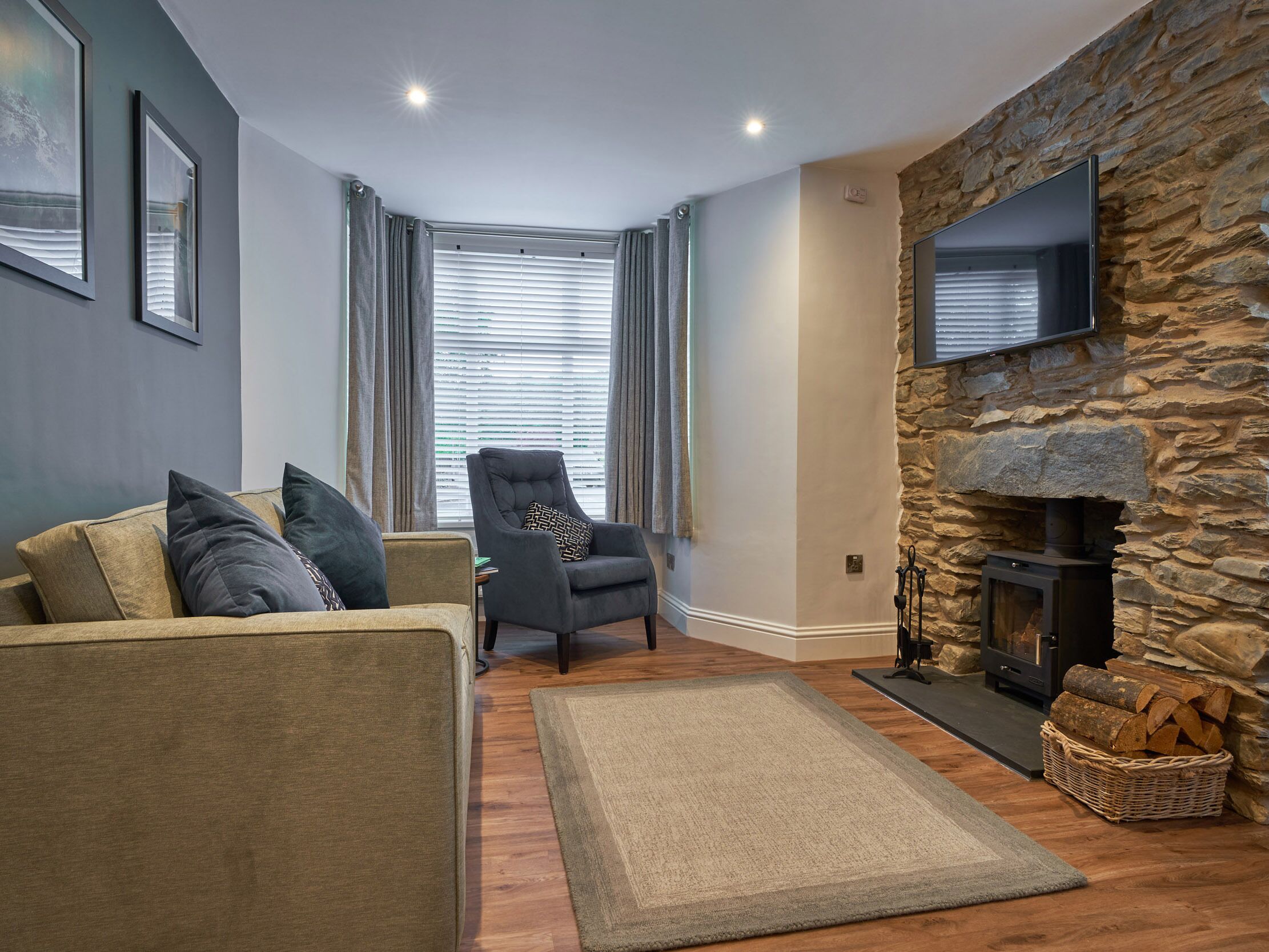 A cozy living room with a stone fireplace, a grey armchair, and a sofa with cushions.