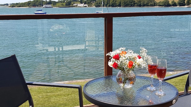 A deck with a table and chairs overlooking a body of water, with boats in the distance. - Delfryd (Y Felinheli)