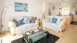 A modern living room with two sofas, a glass coffee table, and a dining area with a kitchen in the background. - Delfryd (Y Felinheli)