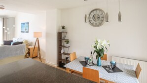 A modern living room with a dining area, featuring a round wall clock, pendant lights, and a potted plant. - Delfryd (Y Felinheli)