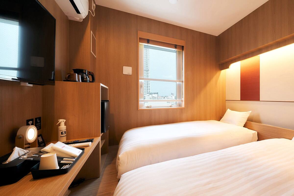 Une chambre d’hôtel avec deux lits, une télévision, un bureau avec une lampe, une fenêtre et une vue sur la ville.