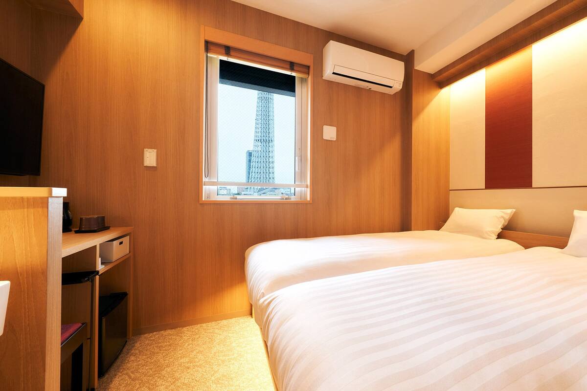 Une chambre d’hôtel avec deux lits, une télévision, une fenêtre donnant sur la ville et un appareil de climatisation.