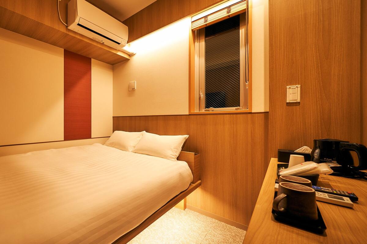 Une chambre d’hôtel avec un lit, un bureau doté d’une machine à café, une télécommande et une fenêtre avec des stores.