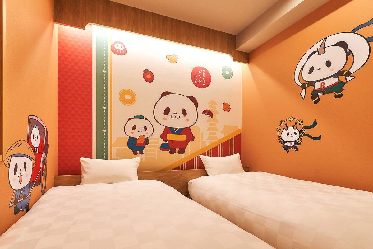 Une chambre d’hôtel avec deux lits, un grand décor mural représentant un panda et des personnages de dessins animés.