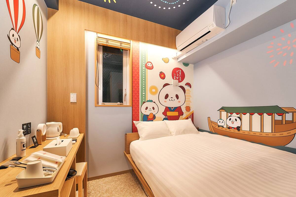 Une chambre d’hôtel comprenant un lit, un bureau avec des articles de toilette, une fenêtre et des éléments de décoration murale, notamment un panda et un bateau.