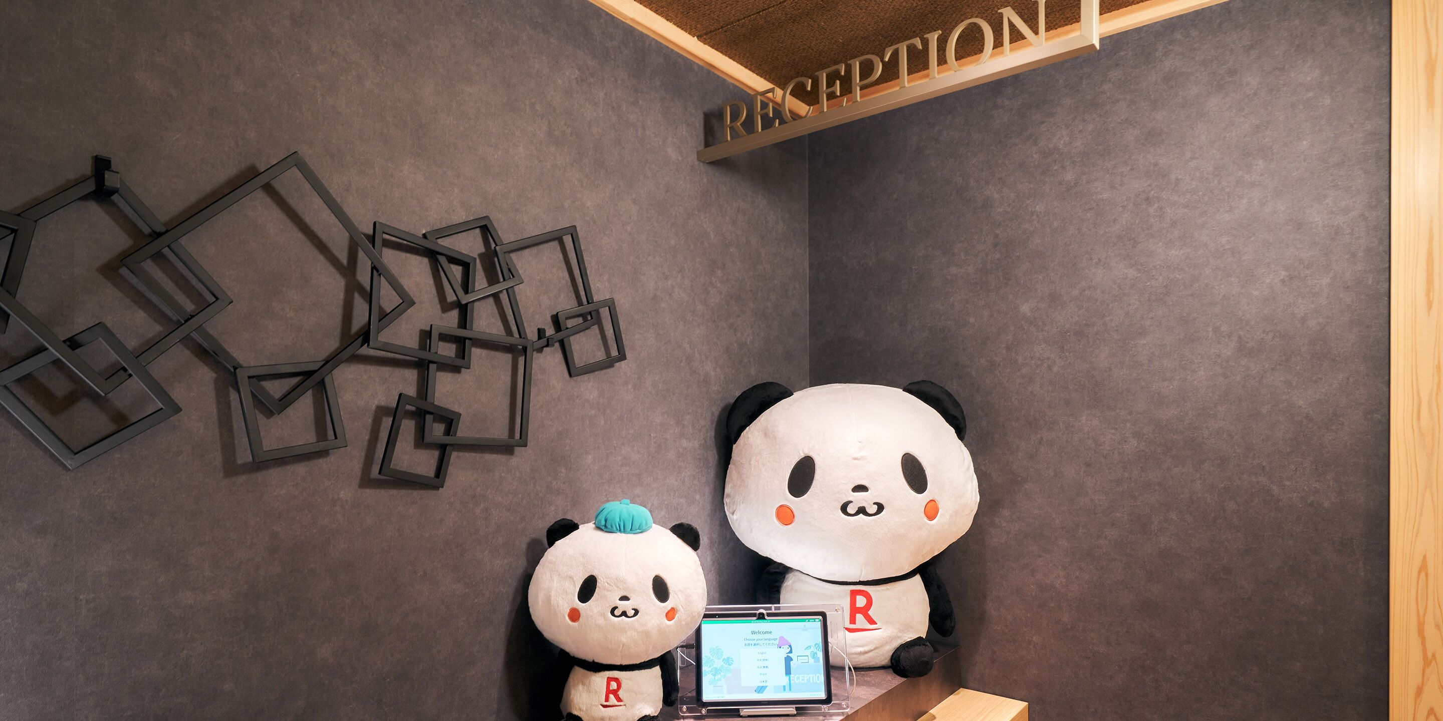 A reception area with a large panda plush toy, a smaller panda plush toy, and a laptop on a table.