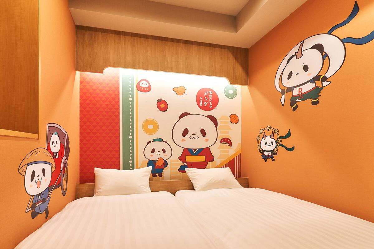 Une chambre d’hôtel équipée d’un lit, d’oreillers, d’une fenêtre et de décorations murales, notamment des personnages de dessins animés.