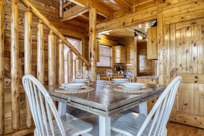 Ein Interieur einer Holzhütte mit einem Esstisch für vier Personen, weißen Stühlen und Holzwänden.