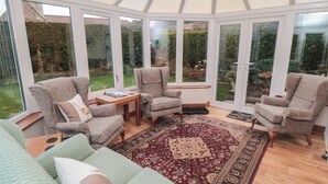 A conservatory with a wooden floor, a patterned rug, and a green sofa with cushions. - Applegarth (Scarborough)