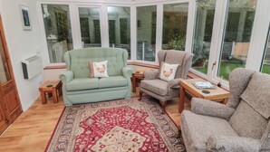 A conservatory with a red patterned rug, two sofas, and a wooden table. - Applegarth (Scarborough)