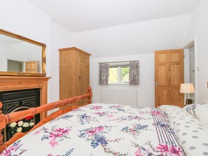 A bedroom with a wooden bed frame, a large mirror, a wooden wardrobe, a window with curtains, and a radiator. - Applegarth (Scarborough)