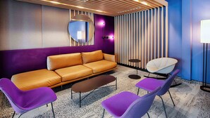 A modern lounge area with a sofa, two purple chairs, a coffee table, and a round mirror on the wall.