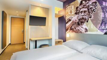 A hotel room with a bed, a desk, a flat-screen TV, and a wall mural.